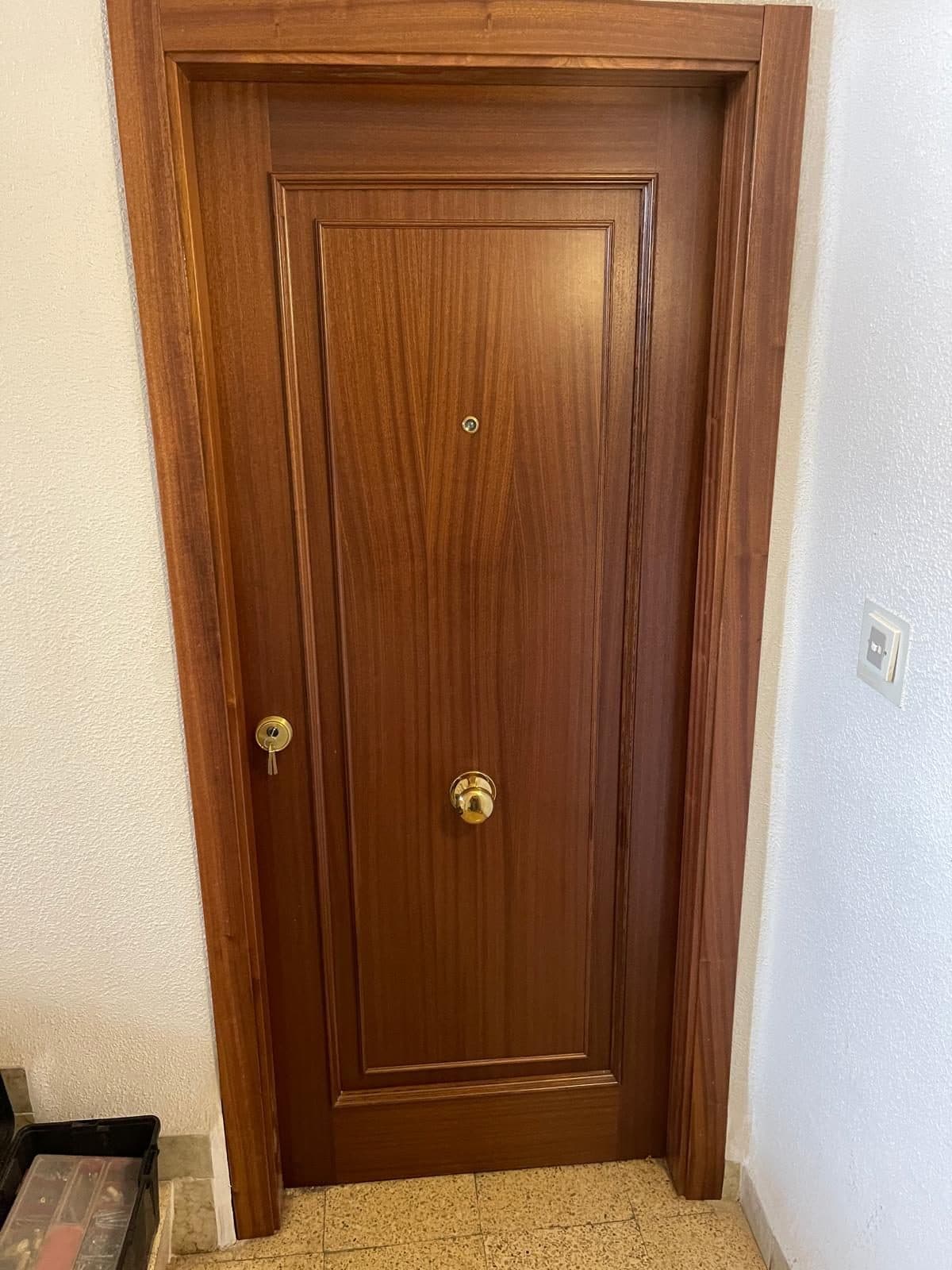 Puerta blindada de madera oscura con pomo de latón en un rellano